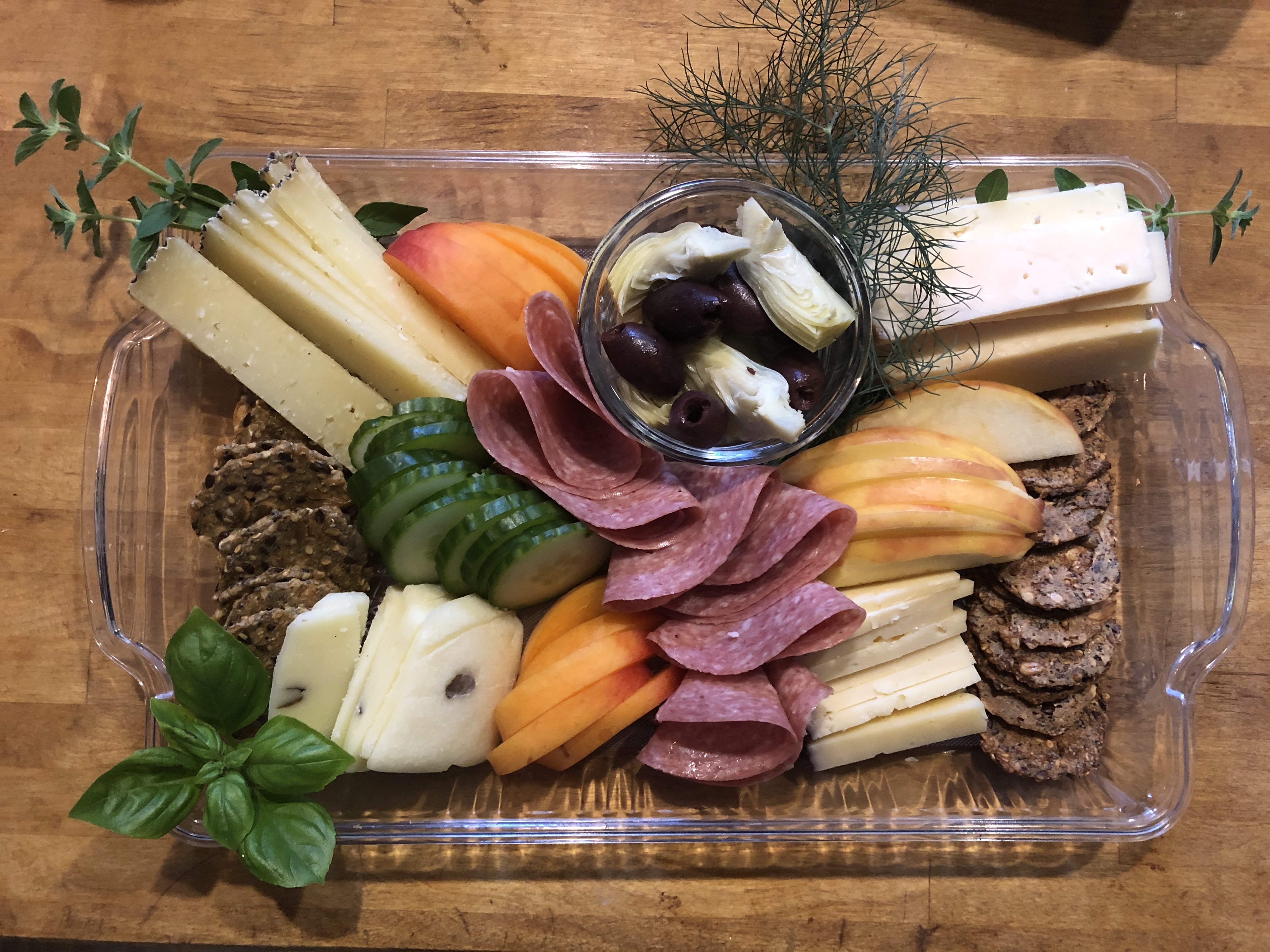 A cheese board on wood with crackers, cheeses, and herbs.