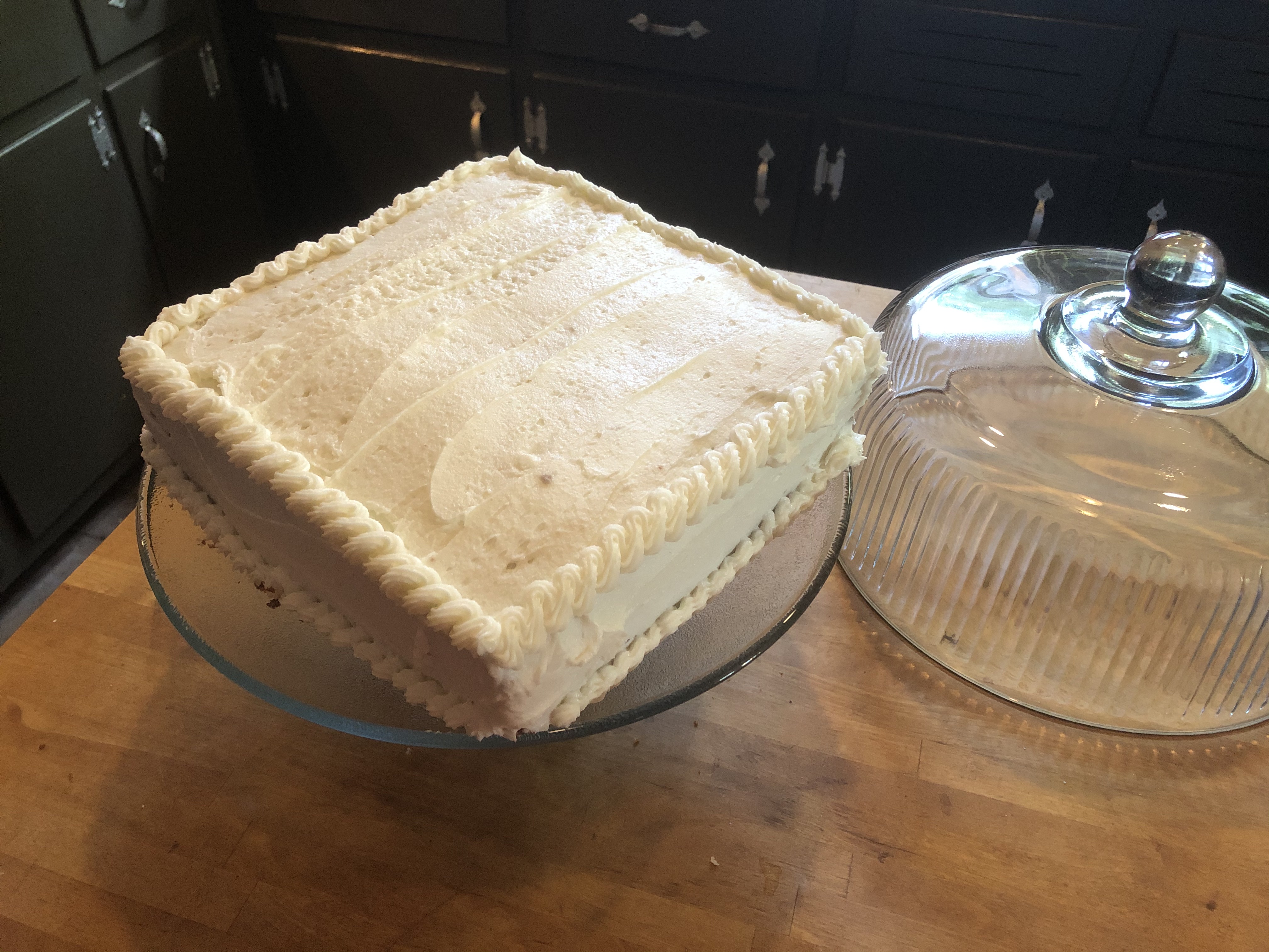 A square white frosted cake on a round cake plate